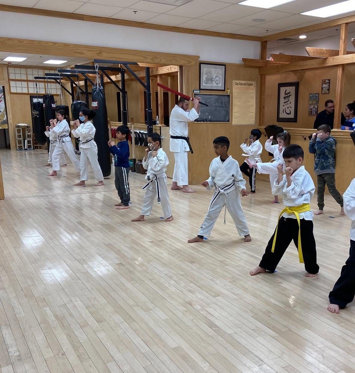 A kids class at the Old Bridge dojo practices a guard stance in rows across the wood floor.